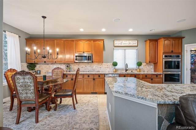 kitchen with tasteful backsplash, light stone countertops, a sink, a chandelier, and stainless steel appliances