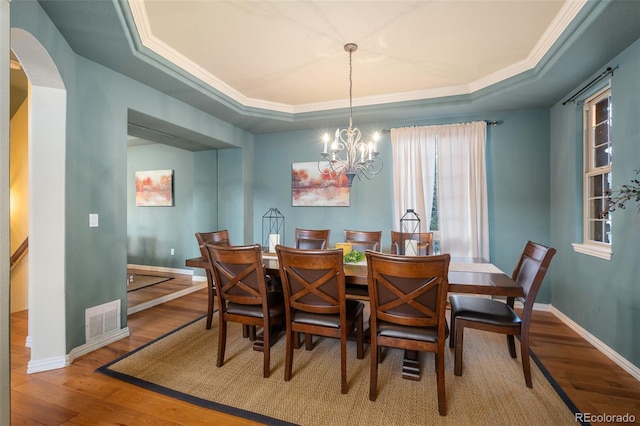 dining room featuring an inviting chandelier, a raised ceiling, baseboards, wood finished floors, and visible vents
