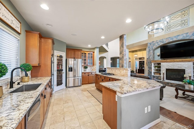 kitchen featuring brown cabinetry, glass insert cabinets, open floor plan, a sink, and appliances with stainless steel finishes