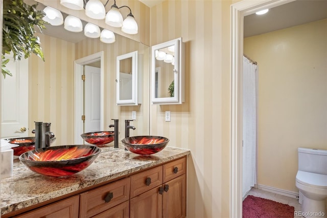 full bathroom with toilet, wallpapered walls, and a sink