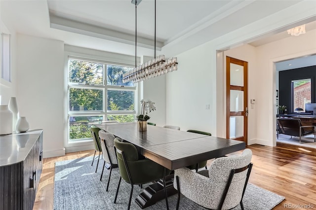 dining area featuring light hardwood / wood-style floors, a raised ceiling, a healthy amount of sunlight, and an inviting chandelier