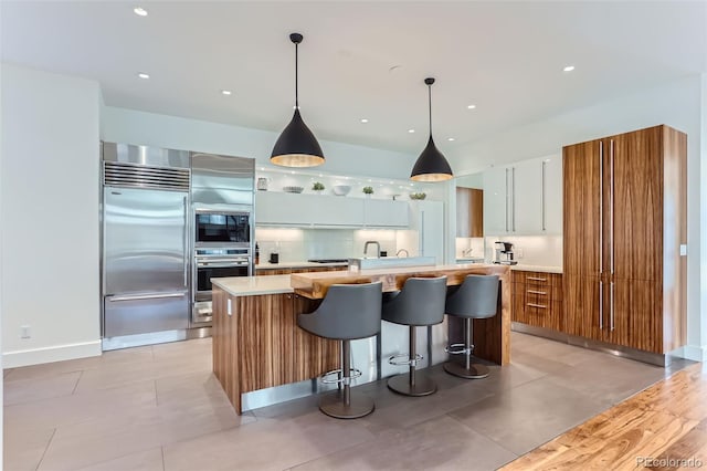 kitchen featuring built in appliances, a kitchen island, white cabinetry, and hanging light fixtures