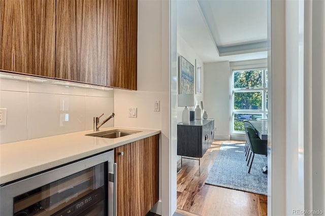 bar featuring backsplash, a raised ceiling, sink, light wood-type flooring, and beverage cooler