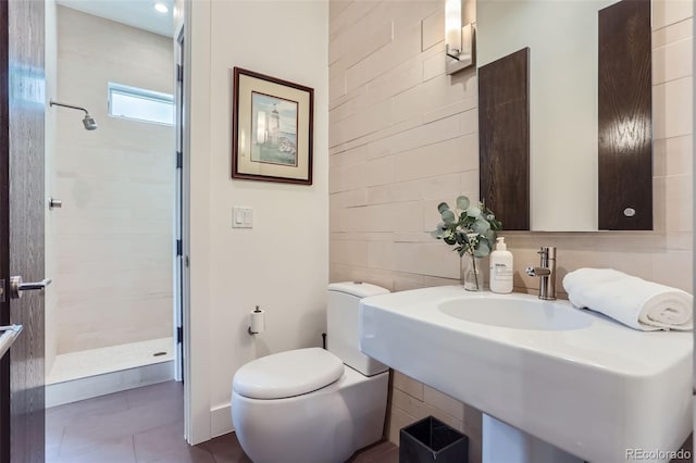 bathroom with toilet, a tile shower, and sink