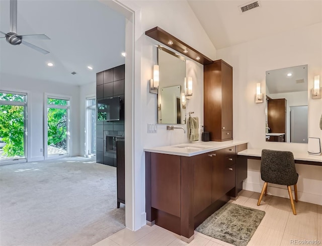 bathroom with a tiled fireplace, ceiling fan, vanity, and lofted ceiling