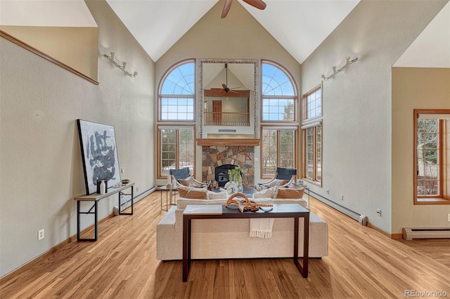 living area featuring baseboard heating, high vaulted ceiling, a stone fireplace, and wood finished floors