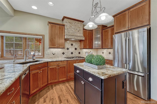 kitchen with light wood-type flooring, light stone counters, brown cabinets, appliances with stainless steel finishes, and a sink