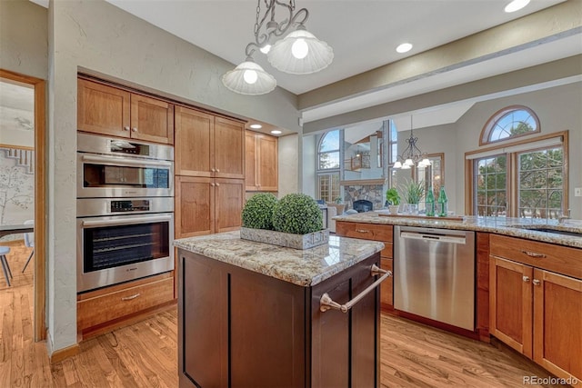 kitchen with a center island, light stone counters, light wood-style flooring, appliances with stainless steel finishes, and hanging light fixtures