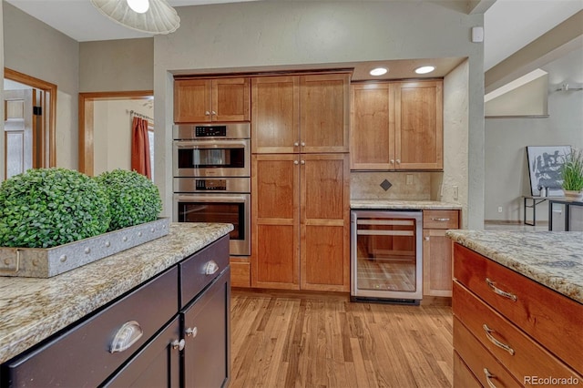 kitchen featuring beverage cooler, double oven, light stone counters, light wood-style flooring, and brown cabinetry