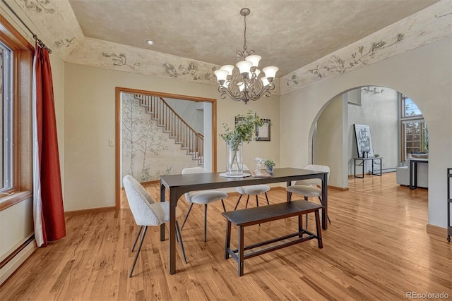 dining room with light wood-style flooring, arched walkways, a baseboard radiator, baseboards, and stairs