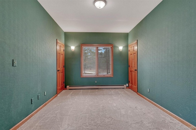 carpeted spare room with a baseboard radiator, baseboards, and a textured wall