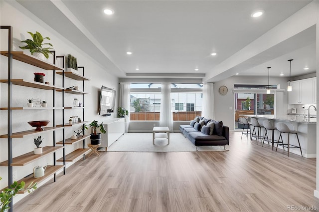 living room featuring light wood-type flooring, sink, and plenty of natural light