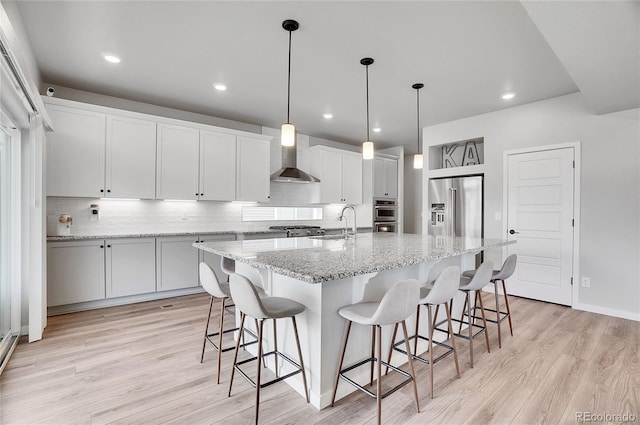 kitchen with a kitchen island with sink, stainless steel appliances, wall chimney range hood, and white cabinets