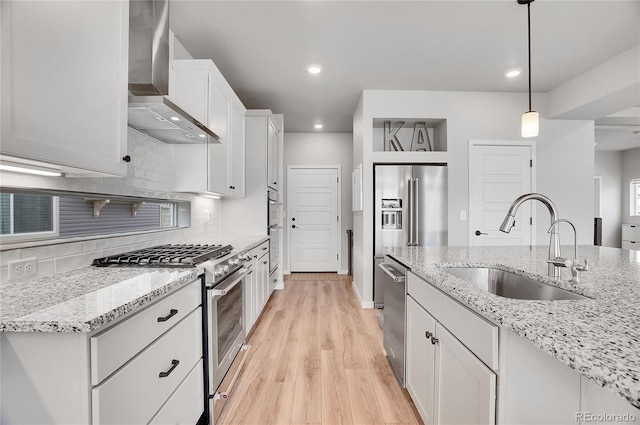 kitchen with white cabinets, appliances with stainless steel finishes, sink, wall chimney exhaust hood, and decorative light fixtures