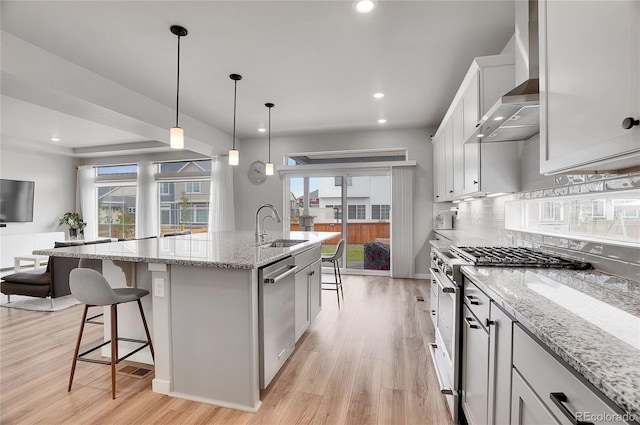 kitchen with appliances with stainless steel finishes, white cabinets, a center island with sink, and light hardwood / wood-style floors