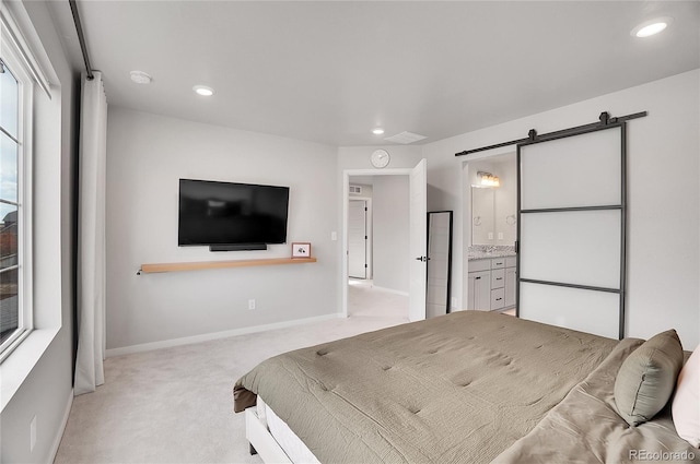 bedroom featuring ensuite bath, light carpet, and a barn door