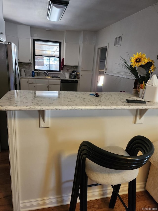 kitchen with white cabinets, a breakfast bar, decorative backsplash, and dishwashing machine