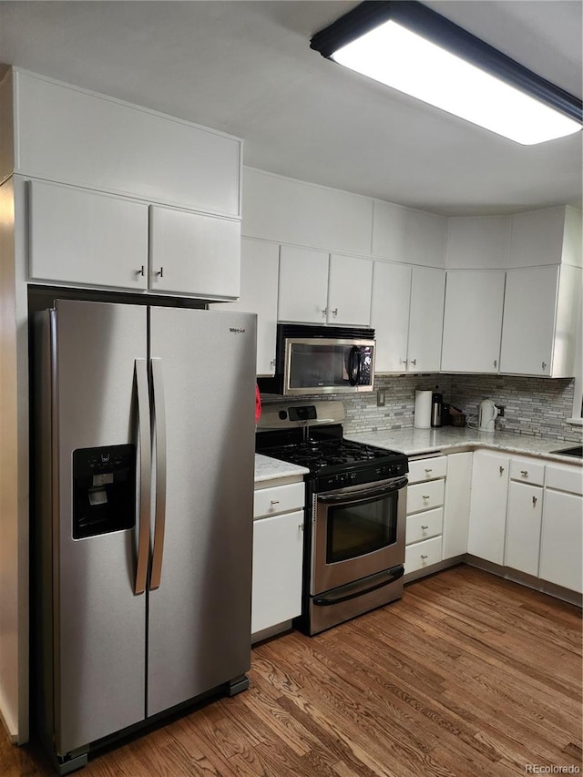 kitchen with appliances with stainless steel finishes, dark wood-type flooring, white cabinetry, and tasteful backsplash