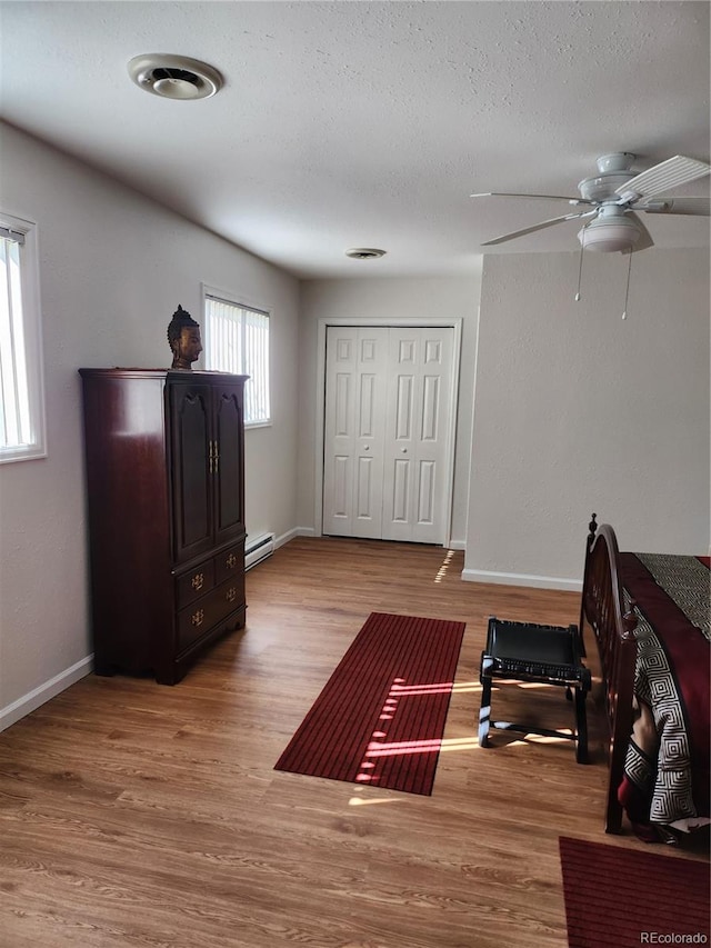 workout area with a textured ceiling, ceiling fan, and light hardwood / wood-style flooring