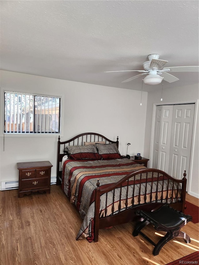 bedroom featuring a baseboard heating unit, ceiling fan, a closet, and hardwood / wood-style floors