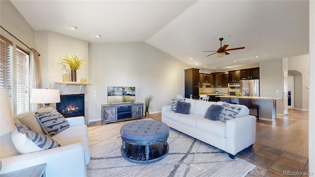 living room with ceiling fan, lofted ceiling, and a tiled fireplace