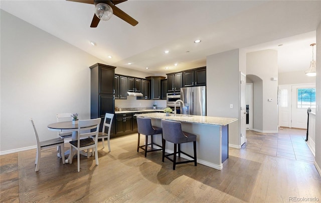 kitchen with arched walkways, light wood-style flooring, a kitchen island with sink, vaulted ceiling, and stainless steel fridge with ice dispenser