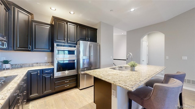 kitchen featuring appliances with stainless steel finishes, a breakfast bar, an island with sink, sink, and light hardwood / wood-style floors