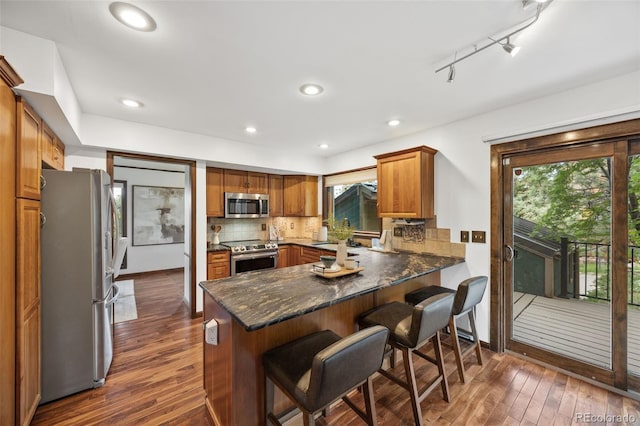 6207 Elbert Pl, Parker, CO 80134 - kitchen with stainless steel appliances, a peninsula, dark wood-style flooring, decorative backsplash, and brown cabinetry