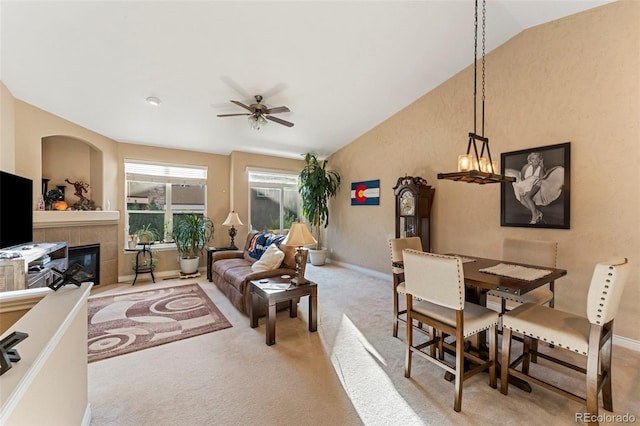 living room featuring ceiling fan with notable chandelier, lofted ceiling, a tile fireplace, and light carpet