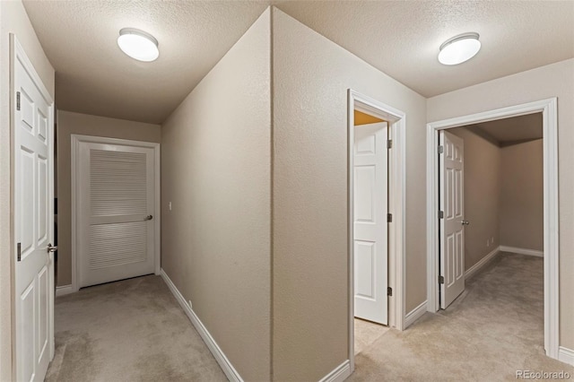 hall featuring a textured ceiling and light colored carpet