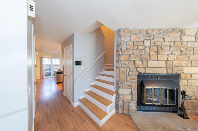 stairway with a stone fireplace and wood-type flooring