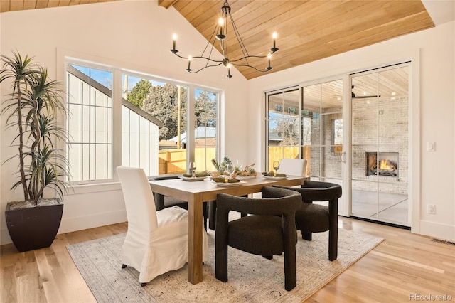 dining area featuring light wood-type flooring, lofted ceiling with beams, a large fireplace, and wood ceiling