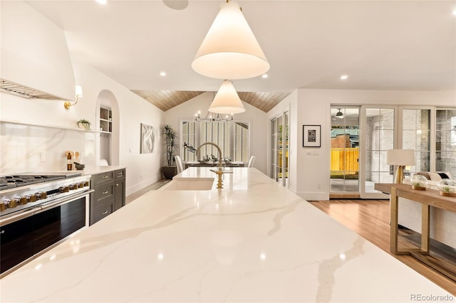 kitchen with light stone countertops, sink, pendant lighting, extractor fan, and stainless steel stove