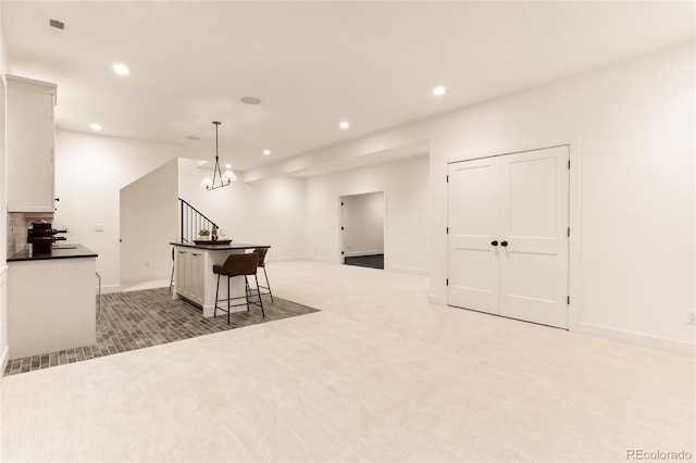 kitchen with white cabinetry, a center island, light colored carpet, decorative light fixtures, and a breakfast bar area