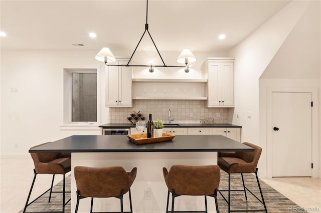 kitchen with decorative backsplash, a kitchen breakfast bar, sink, a center island, and white cabinetry