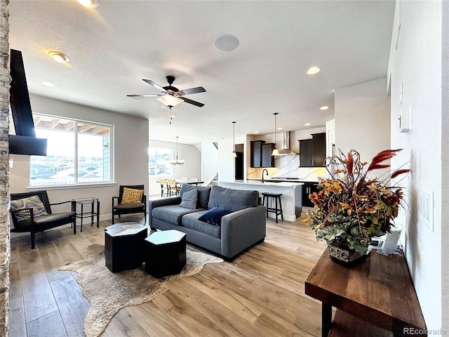 living room with light wood-type flooring, a textured ceiling, sink, and ceiling fan