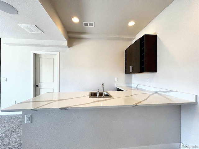 kitchen with light stone countertops, kitchen peninsula, carpet flooring, and sink