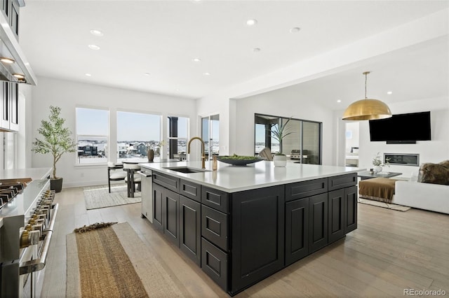 kitchen with sink, decorative light fixtures, a center island with sink, light wood-type flooring, and appliances with stainless steel finishes