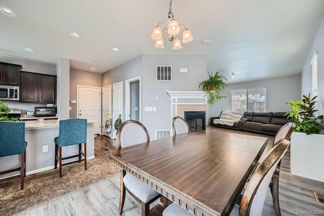 dining space with a fireplace, light hardwood / wood-style floors, and an inviting chandelier