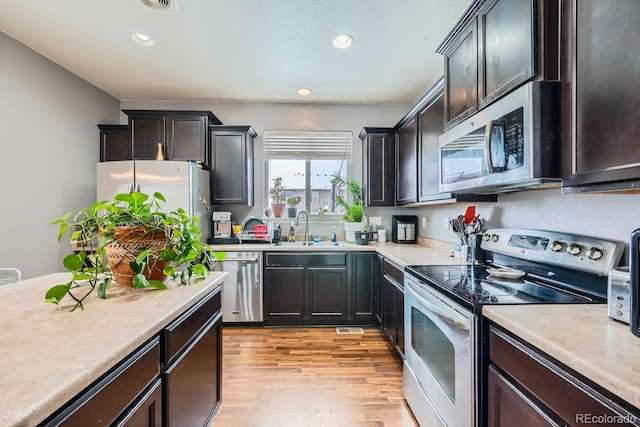 kitchen featuring dark brown cabinetry, sink, light hardwood / wood-style flooring, and appliances with stainless steel finishes