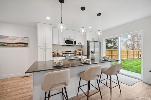 5242 Columbine Ln, Denver, CO 80221 - kitchen with appliances with stainless steel finishes, dark countertops, light wood-type flooring, a breakfast bar, and recessed lighting