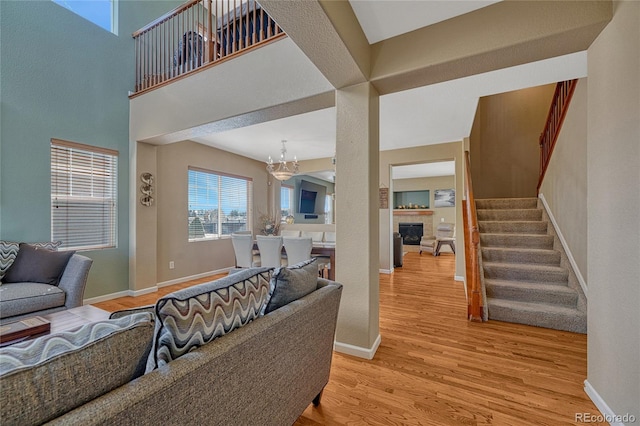 living room featuring stairway, light wood-style floors, a glass covered fireplace, a chandelier, and baseboards