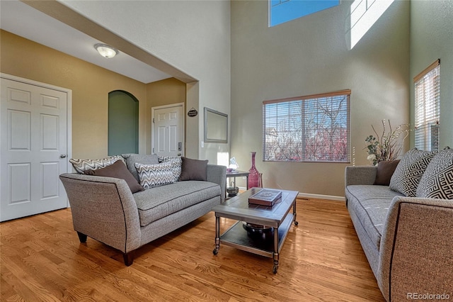 living room with arched walkways, baseboards, a high ceiling, and light wood finished floors