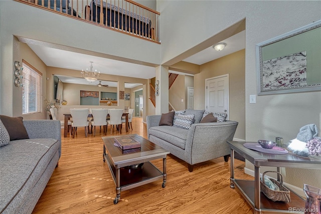 living room featuring light wood-style flooring, a notable chandelier, a towering ceiling, baseboards, and stairs