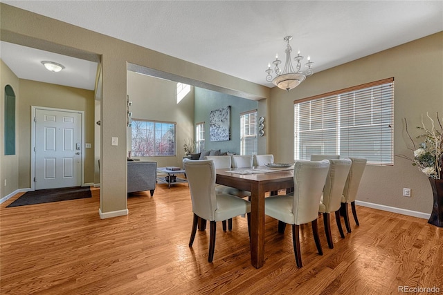 dining room featuring an inviting chandelier, baseboards, arched walkways, and light wood-style floors