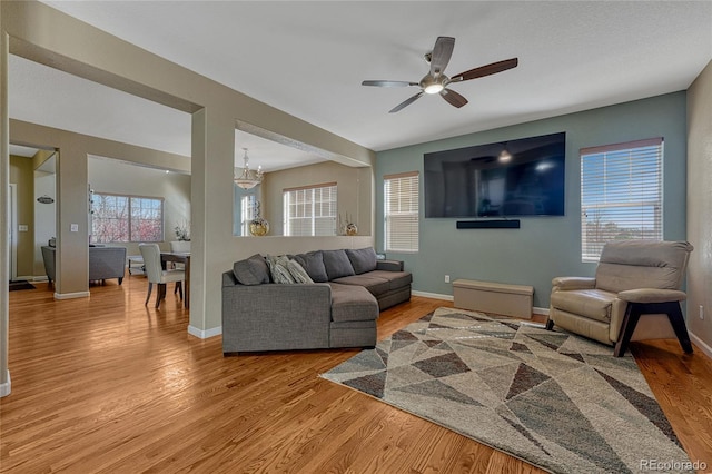 living room featuring ceiling fan with notable chandelier, light wood finished floors, and baseboards