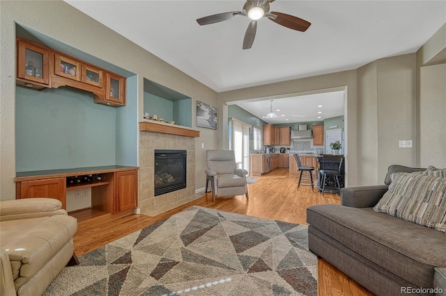 living area with light wood finished floors, a fireplace, and a ceiling fan