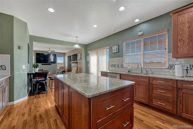 kitchen with light stone counters, light wood-type flooring, a sink, and pendant lighting