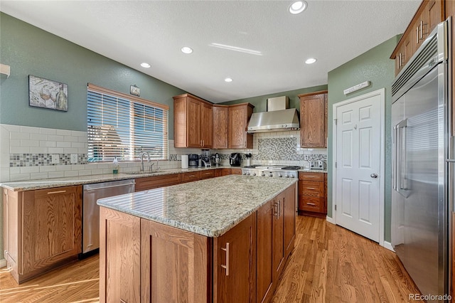 kitchen with light stone counters, a center island, appliances with stainless steel finishes, a sink, and wall chimney exhaust hood