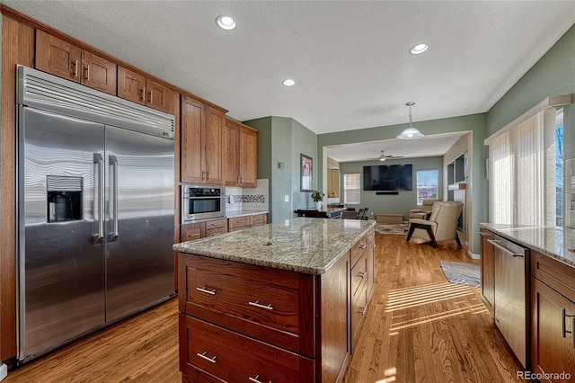 kitchen featuring open floor plan, a center island, hanging light fixtures, light stone countertops, and stainless steel appliances